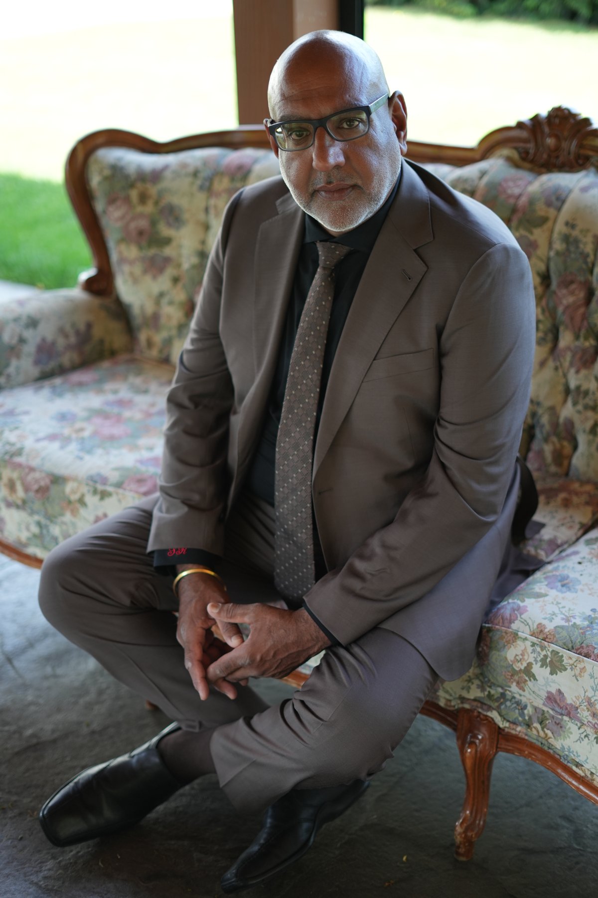 Bespoke tan suit, seated portrait on a vintage floral sofa by Suited Booted & Co.